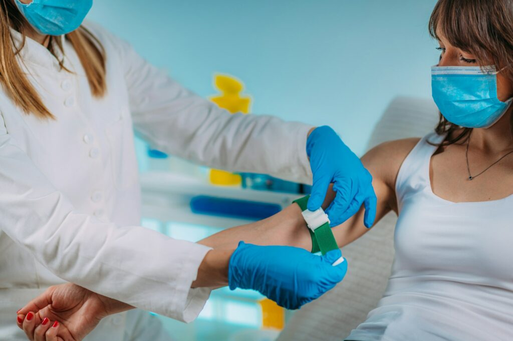 Preparation for phlebotomy procedure, female patient and medical nurse wearing protective masks